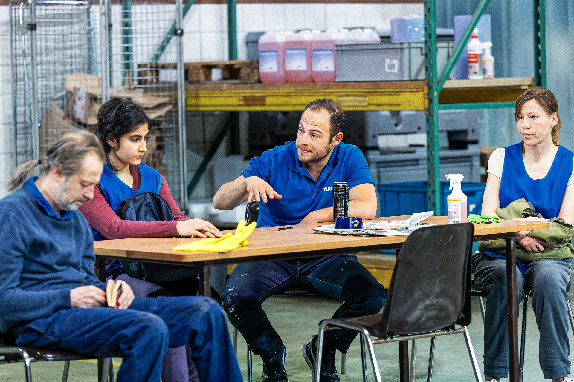 Die beiden Frauen sitzen zusammen mit dem Vorgesetzten an einem Tisch. Der Vorgesetzte hält seine Rede über Erfolgsrezepte und seine spirituellen Vorstellungen, die allein erziehende Mutter entzieht sich. Der Hausmeister ist mit sich selbst beschäftigt. Die beiden Frauen blicken hoffnungslos und kritisch in die Runde. Zu sehen sind weitere Gegenstände wie die gelben Putzhandschuhe, ein Energy Drink mit der Aufschrift Monster und ein Aschenbecher.