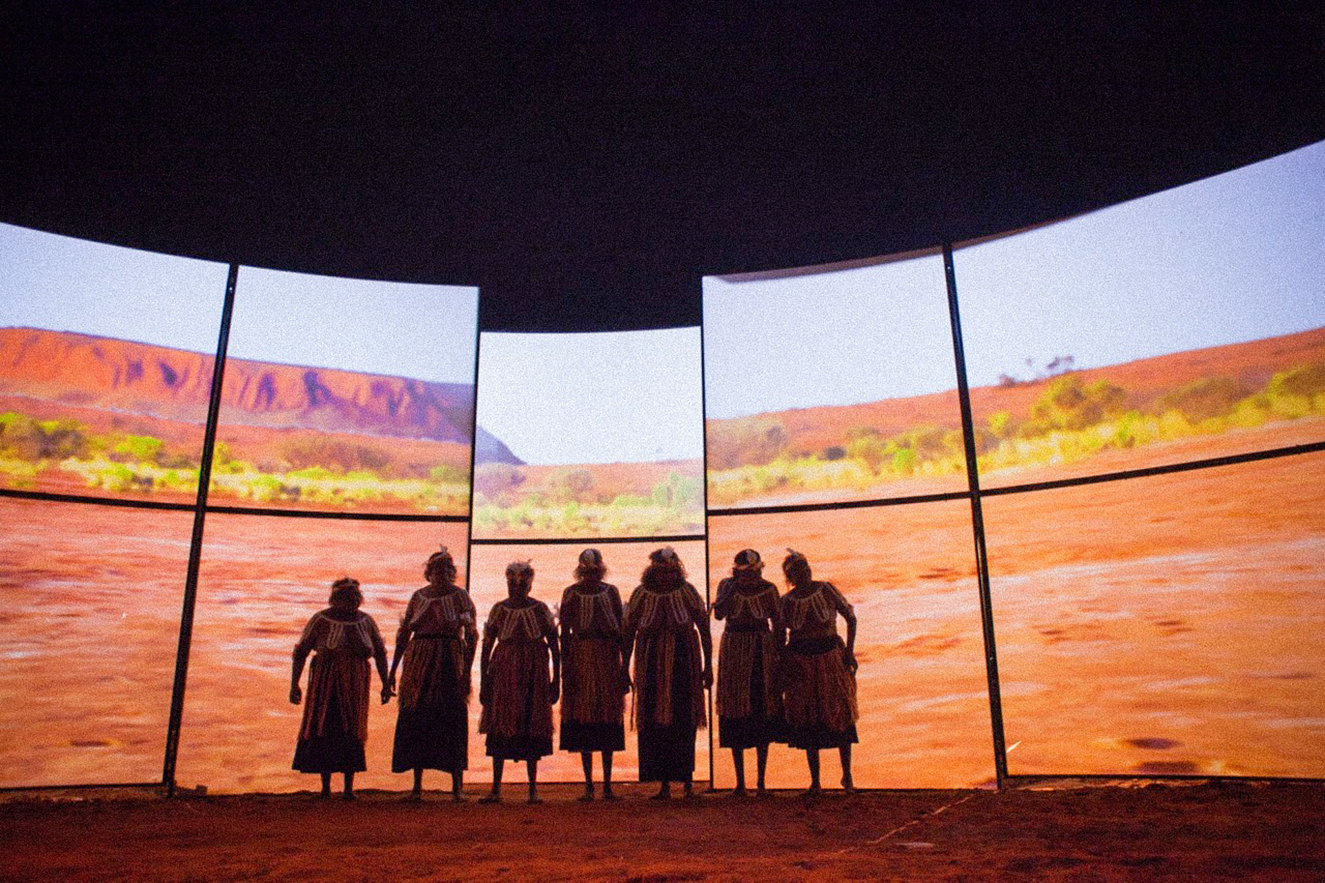 The seven sisters in front of a large screen, showing the dessert of Australia 
