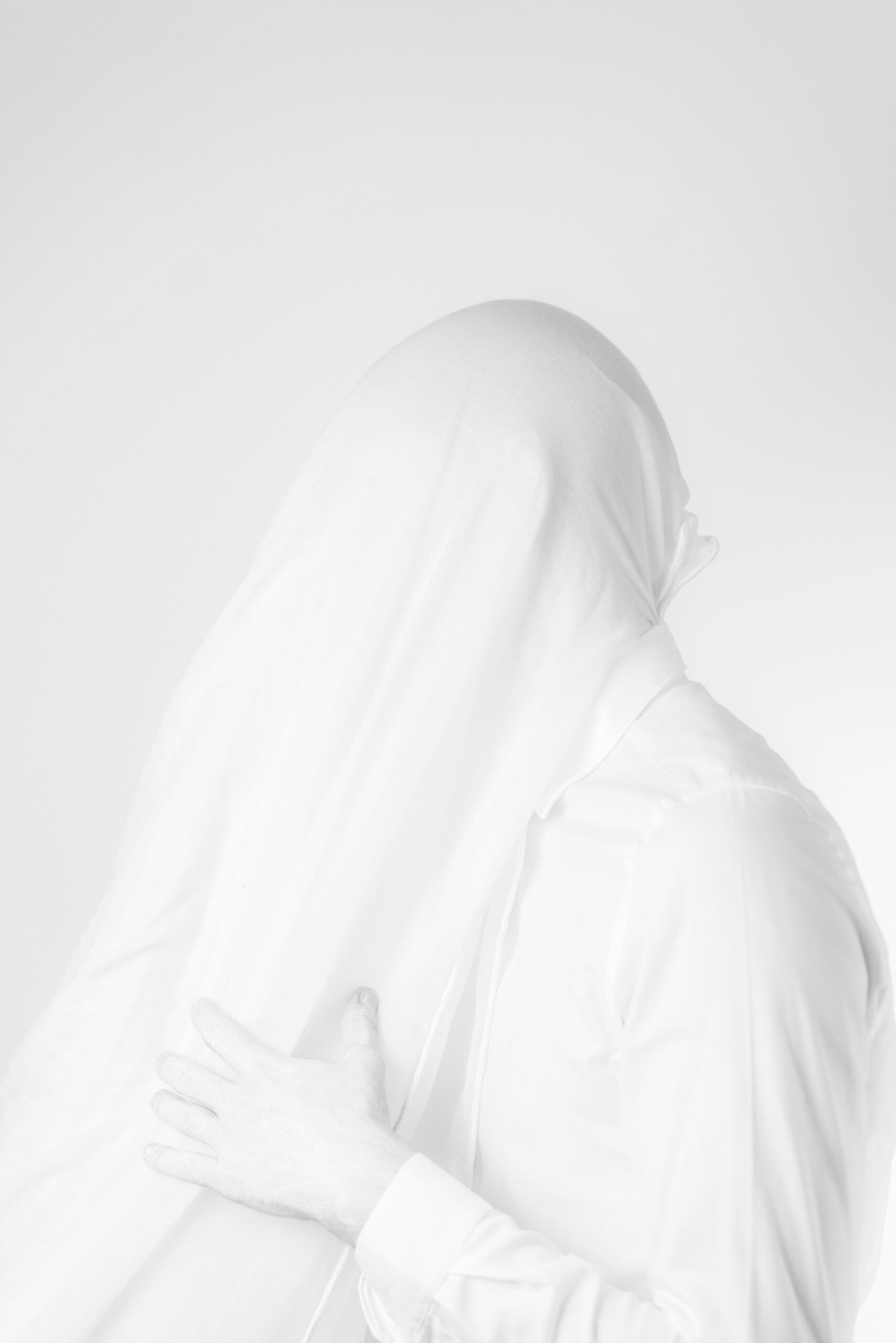 A person veiled in white fabric in front of a matching background.