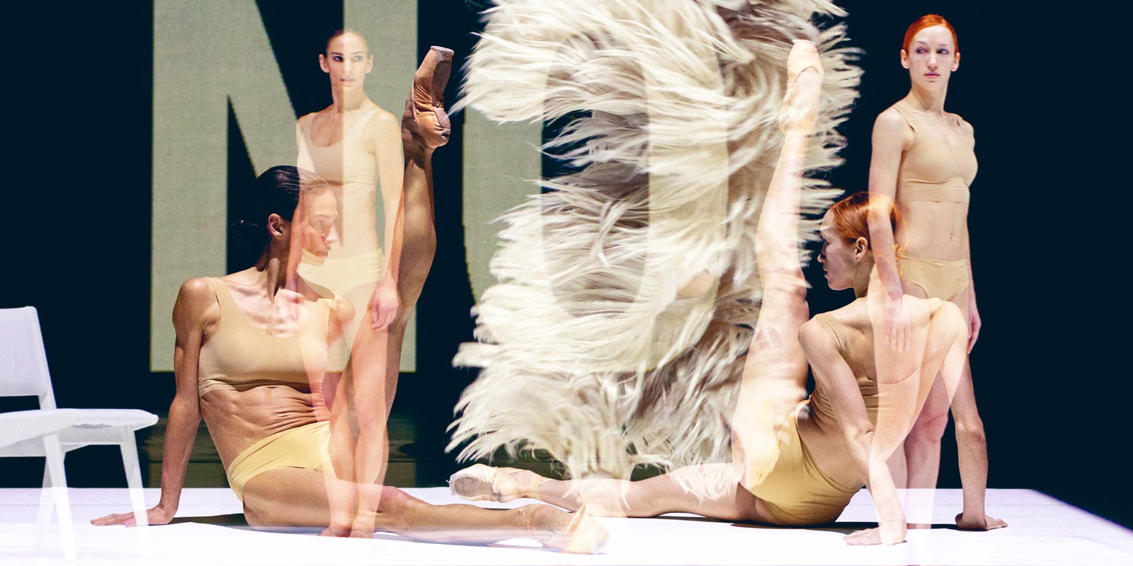 Vier Tänzerinnen auf der Bühne, darüber liegt ein Ausschnitt des Kostüms der  Hauptfigur mit fedrig wirkender Hose und das Wort "NO"