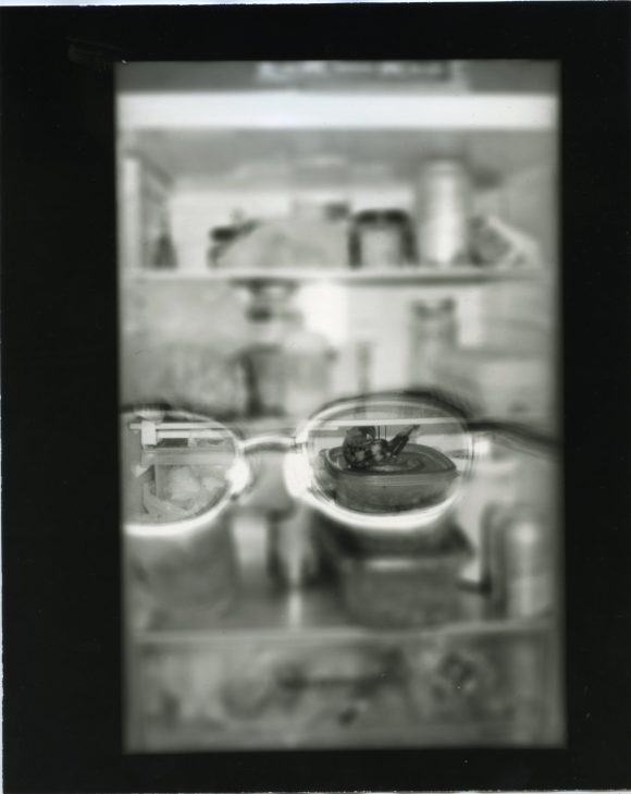 A pair of classes in front of a refrigerator, capturing a plastic box with food through the lense.