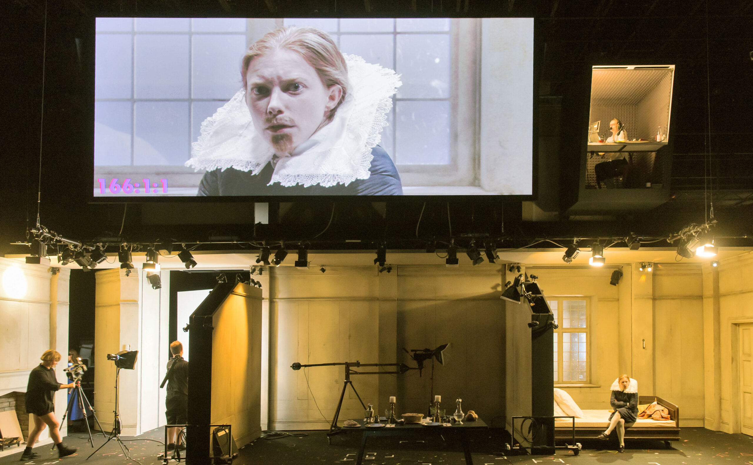 Orlando im Monolog auf einem Screen, darunter zu sehen sind die Bühnenbilder mit einzelnen Räumen und der Videoausstattung.