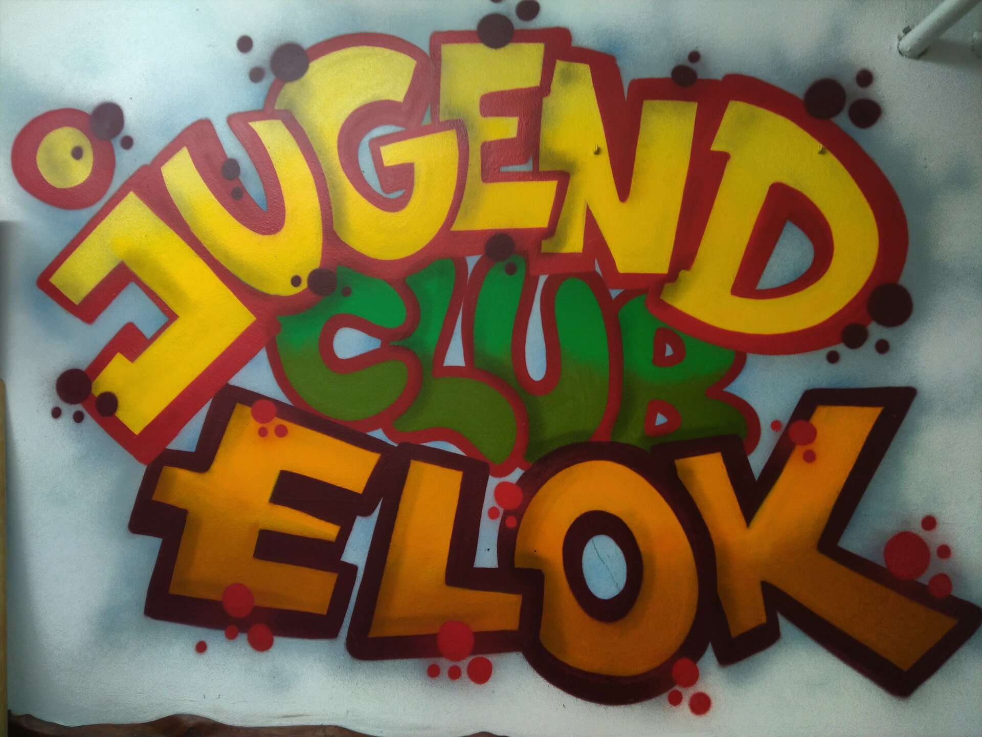 Graffiti an einer Wand des Jugendhauses ELok mit dem Wortlaut "Jugendclub ELok" in orange, rot, gelb, grün und rostrot.