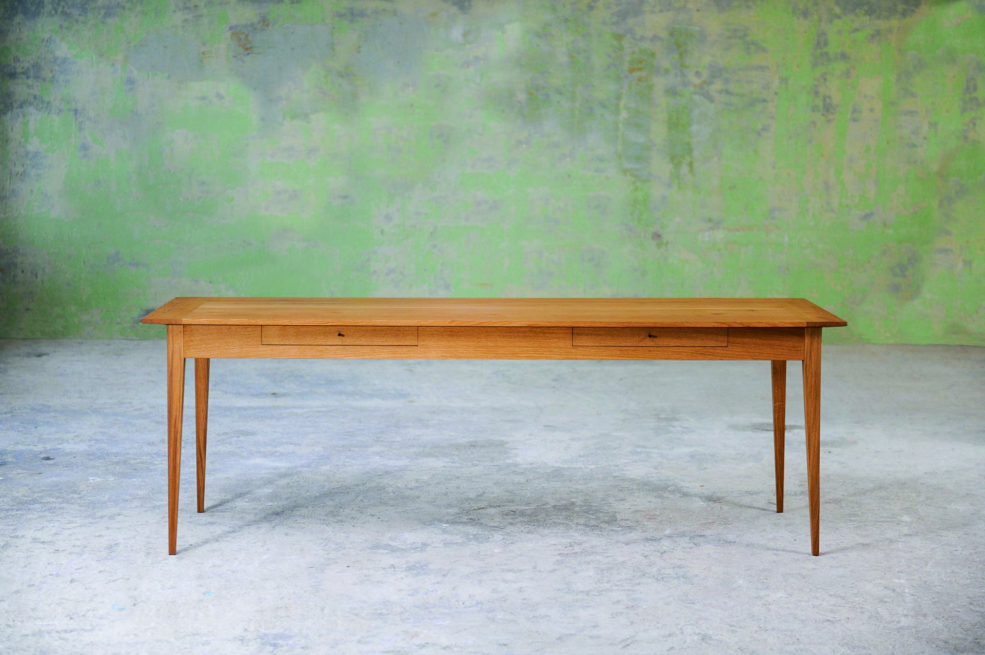 Langer Esstisch aus Holz mit zwei Schubladen und konischen Beinen.