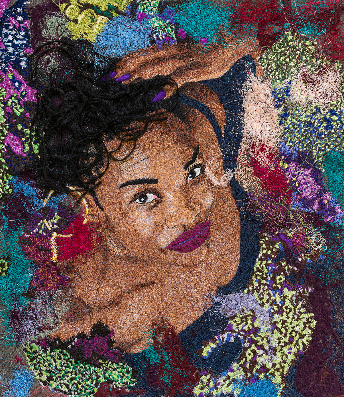 The artist from a top view on an embroidered canvas. She tocuhes her curly hair, her brown eyes are open wide and her lips are captured in a dark purple. The background features a bright mix of colours and abstract patterns.