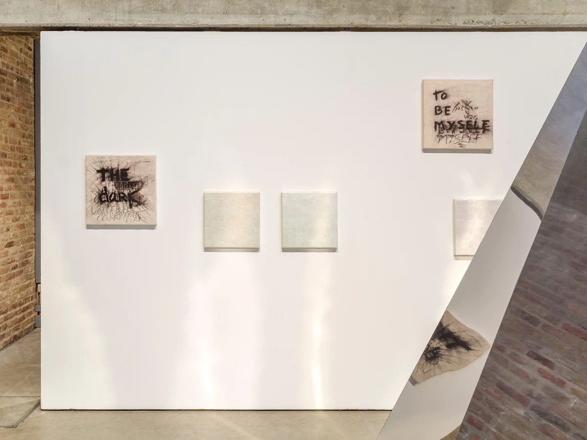 Innerhalb der Galerie, v.l.n.r.: quadratische Gemälde mit der graffitiähnlich gestalteten Aufschrift "The Dark", "To be myself" und vermeintlich weißen Quadraten. Sowie ein Ausschnitt der großformatigen Skulptur in Form eines silbernen Primas. Ebenfalls im Header Image zu sehen.